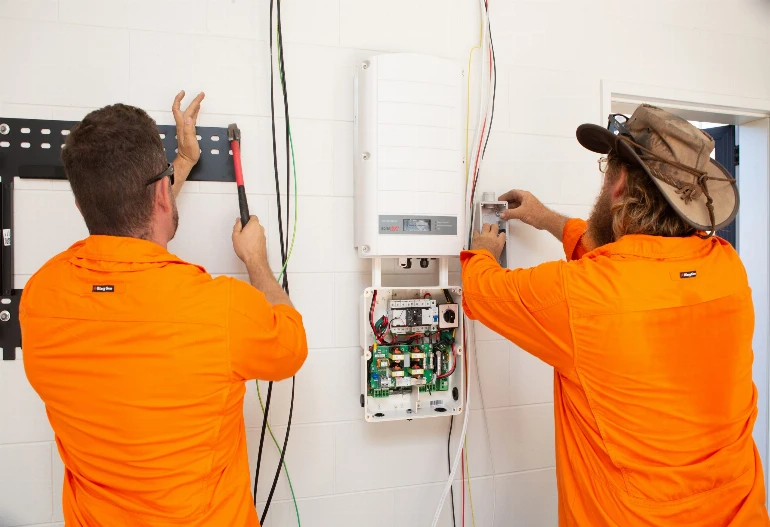 Two men in orange shirts working on a solar power electrical system.