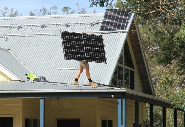 A man standing on the roof of a house harnessing solar power with solar panels in Cairns.